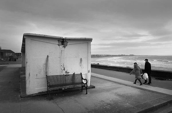 Man and woman walk along the sea front in high winds, Troon