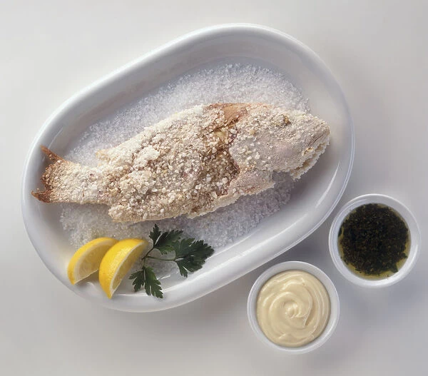 Pescado a la Sal, salted fish served with bowls of mayonnaise and parsley sauce, a typical dish from Southern Spain, view from above