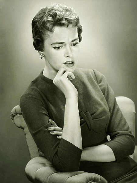 Distraught woman sitting in armchair in studio, (B&W), portrait