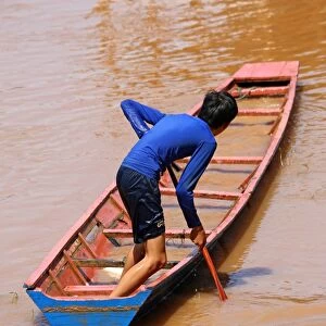 Boy paddling a flooded sinking boat on the Mekong River in Luang Prabang, Laos