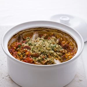 Cassoulet, a traditional dish from Southwest France, containing sausages, beans and tomatoes, topped with breadcrumbs and parsley, baked in a casserole, close-up
