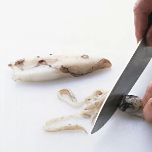 Using small kitchen knife to cut tentacles from head of squid in front of the eyes, close-up