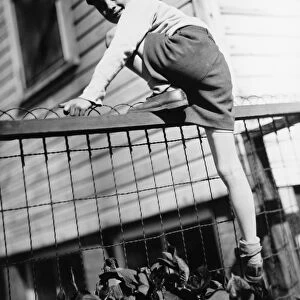 Boy (8-9) climbing on enclosure in front of house, (B&W)