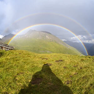 Shadow of a man looking at rainbow over mountain landscape at Kaiser Franz Josefs Hohe in Grossglockner High Alpine Road in the Hohe Tauern National Park, Carinthia, Austria